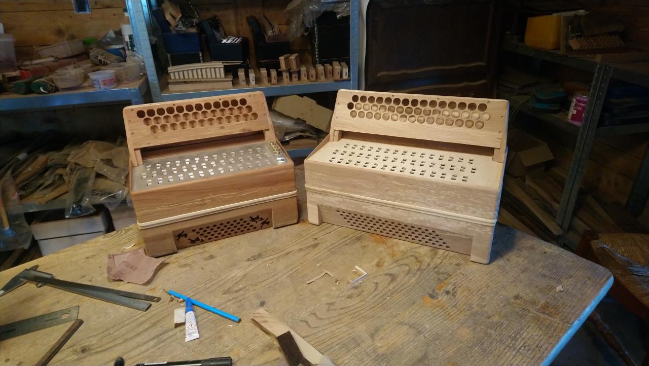 Deux caisses d'accordéons en bois, sans mécanique ni soufflet, posées sur la table d'un atelier.